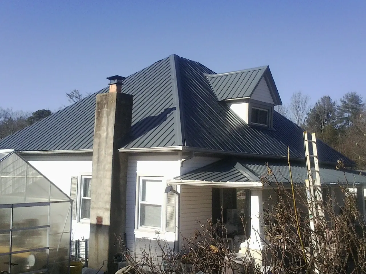 Dark blue standing seam metal roof on a white farmhouse with dormer — Slate & Tile Roof Repair by Roofing Brothers in Alliance