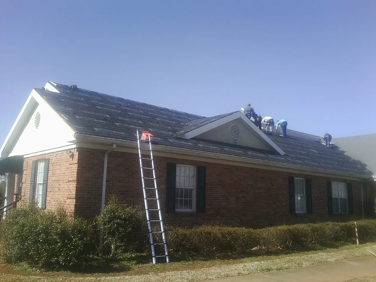Crew tearing shingles off a brick ranch roof with a ladder set — Emergency Roof Repair work by our crew in Alliance