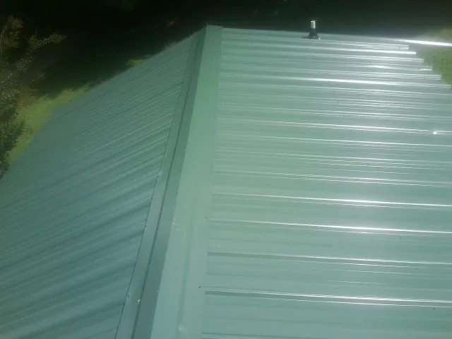 New green metal panels meeting at the ridge of a roof — Flat Roof Repair work by our crew in Alliance