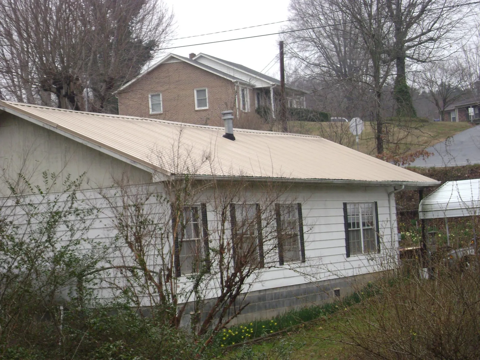 Tan metal roof on a white sided house set into a hillside — Commercial Roofing by Roofing Brothers in Alliance